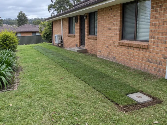 Reinstated lawn trench beside a brick house with a concrete access cover in Kings Langley